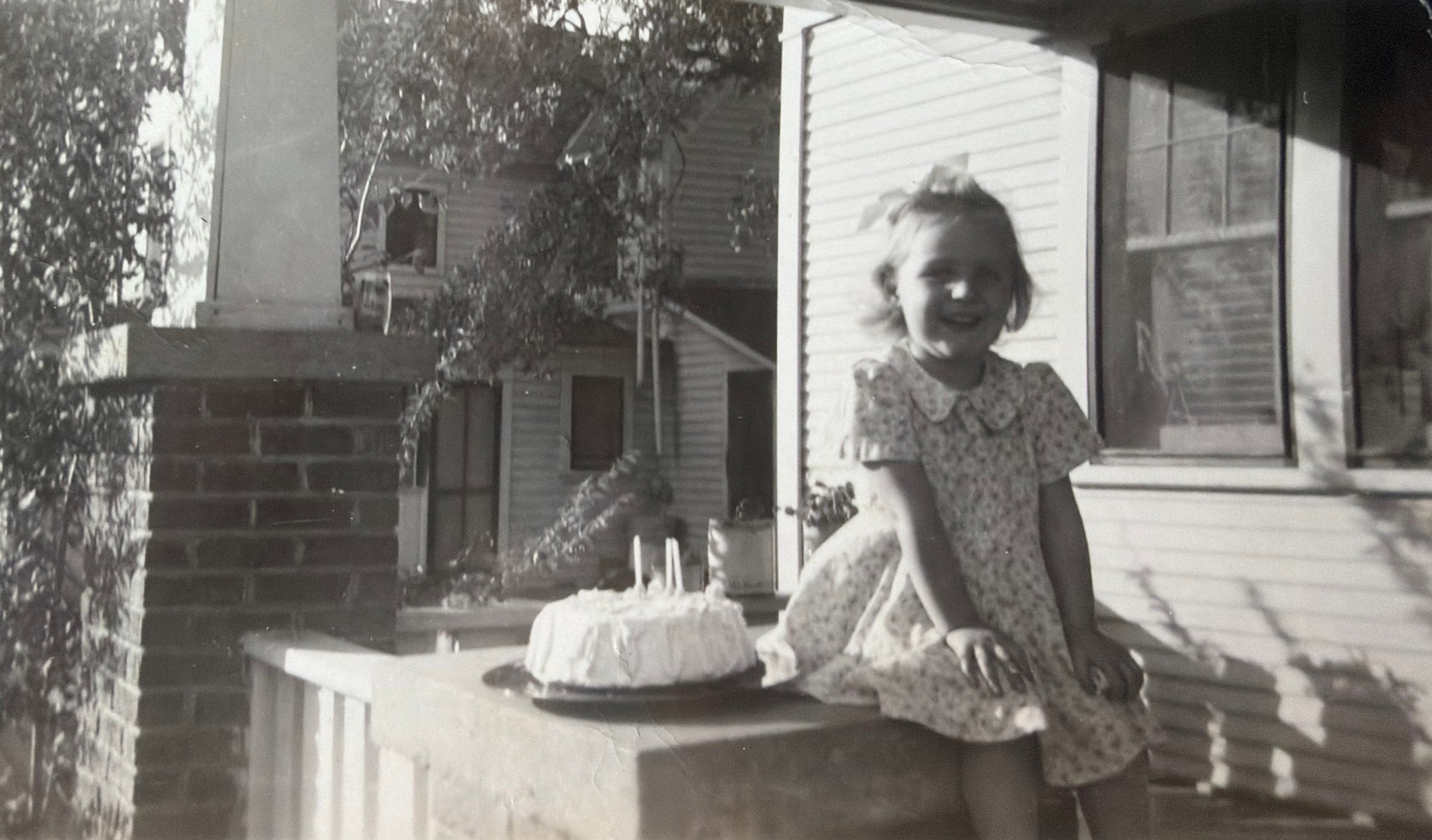 Linda as a child, seated outdoors beside a birthday cake.