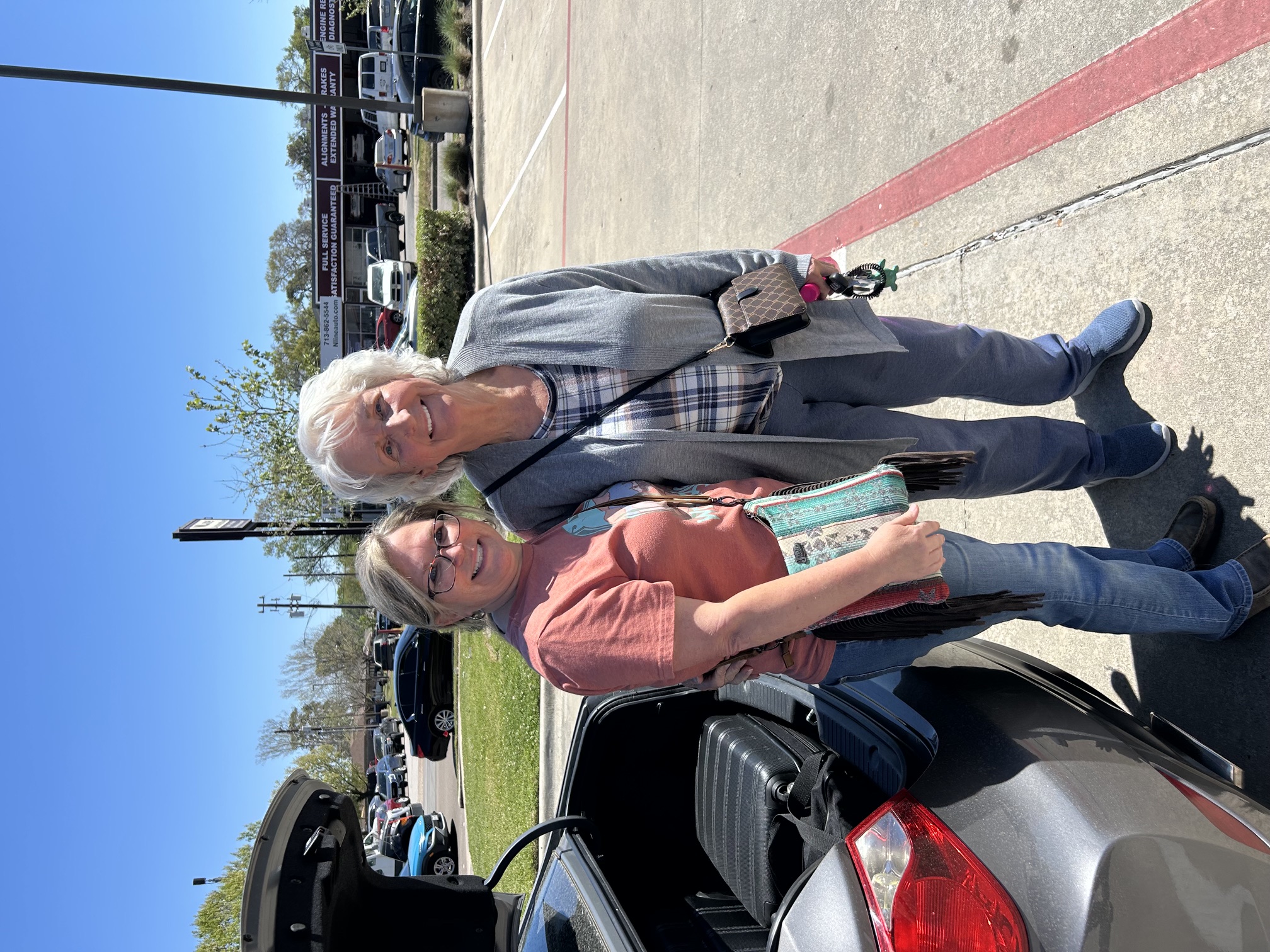 Linda and a woman standing together beside a car on a sunny day.