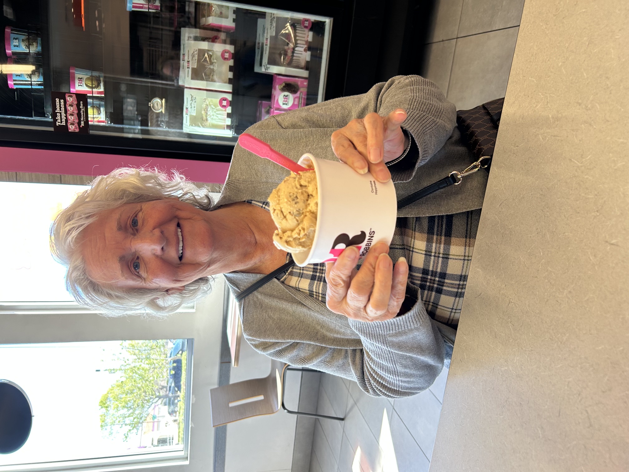 Linda smiling at a table while holding a cup of ice cream.