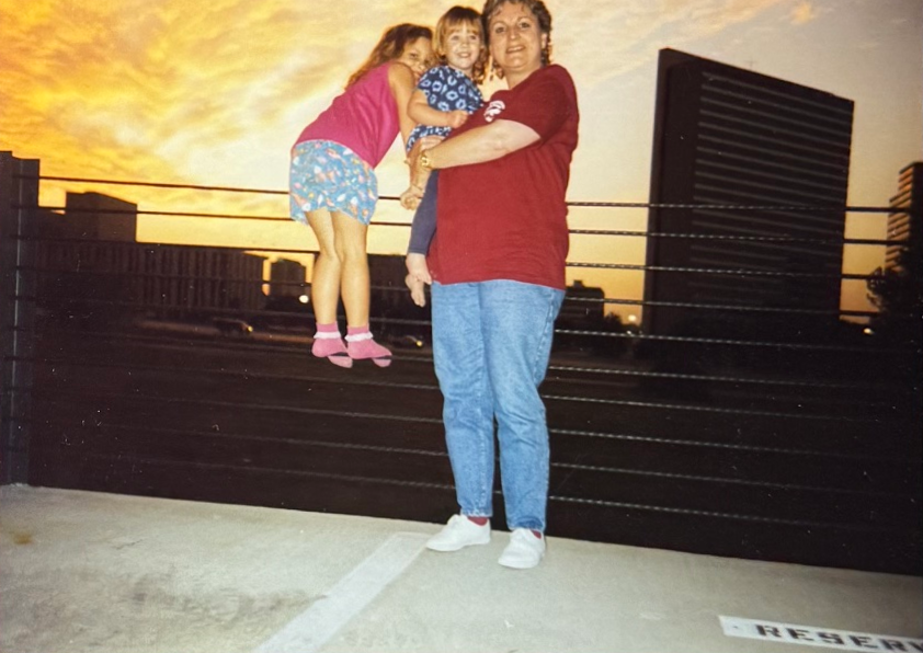 Linda holding two children beneath a colorful evening sky.