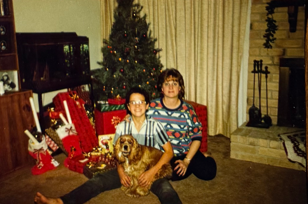 Linda and a boy sitting beside a dog in front of a Christmas tree.