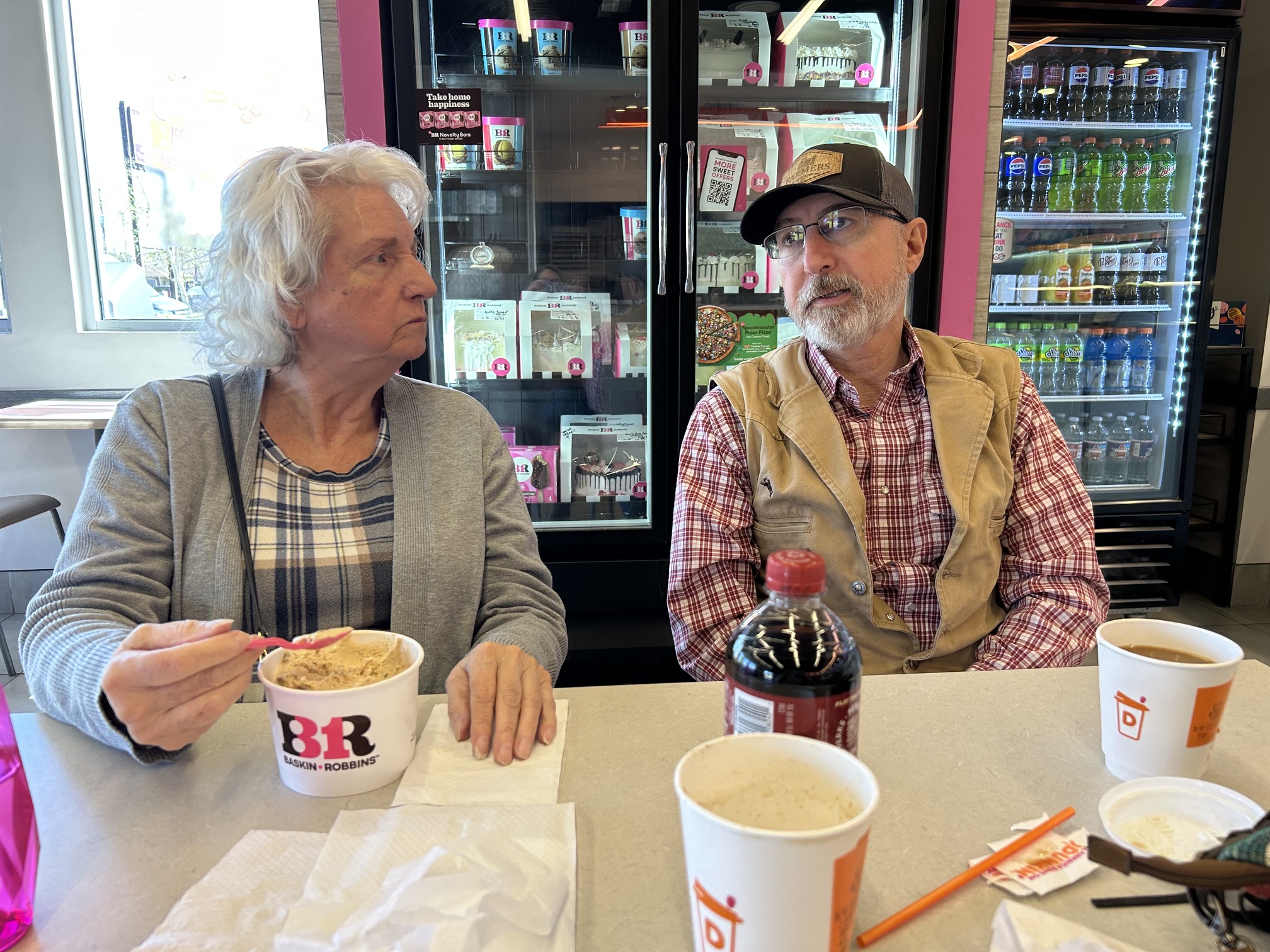 Linda sitting beside a man in a cap, sharing an ice cream outing.