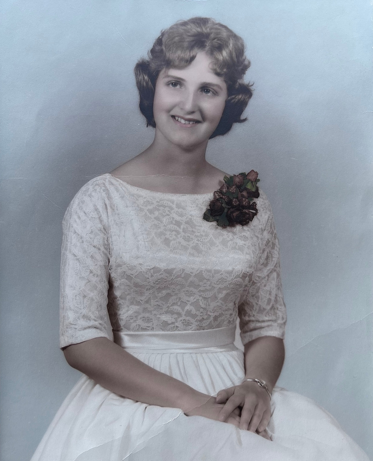 Young Linda seated in a lace dress with a floral corsage, her hands resting in her lap.