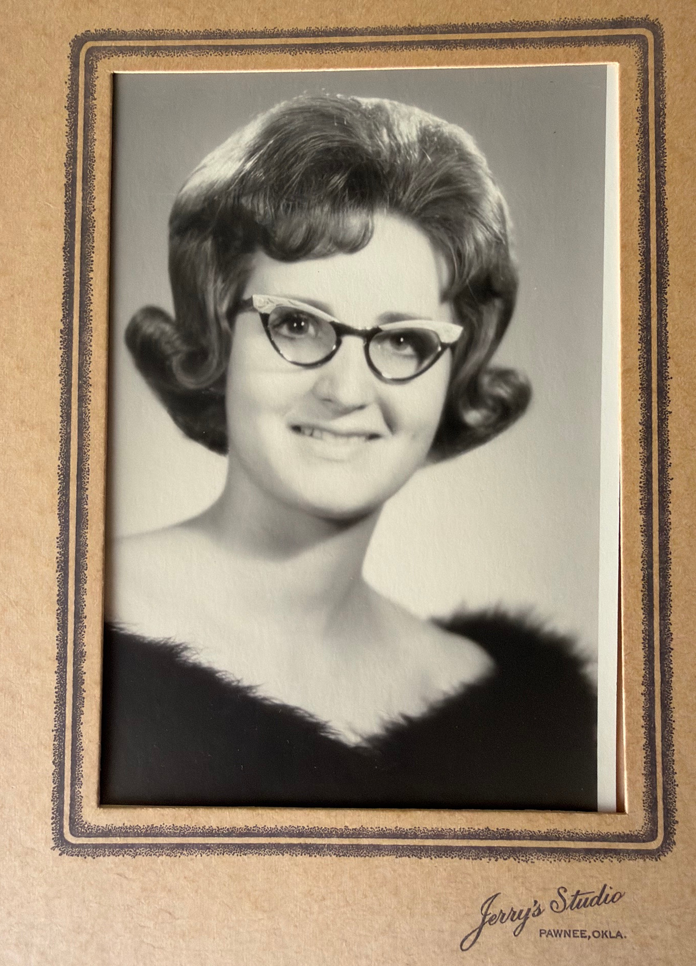 A portrait of young Linda wearing cat-eye glasses, with the original studio lettering below.