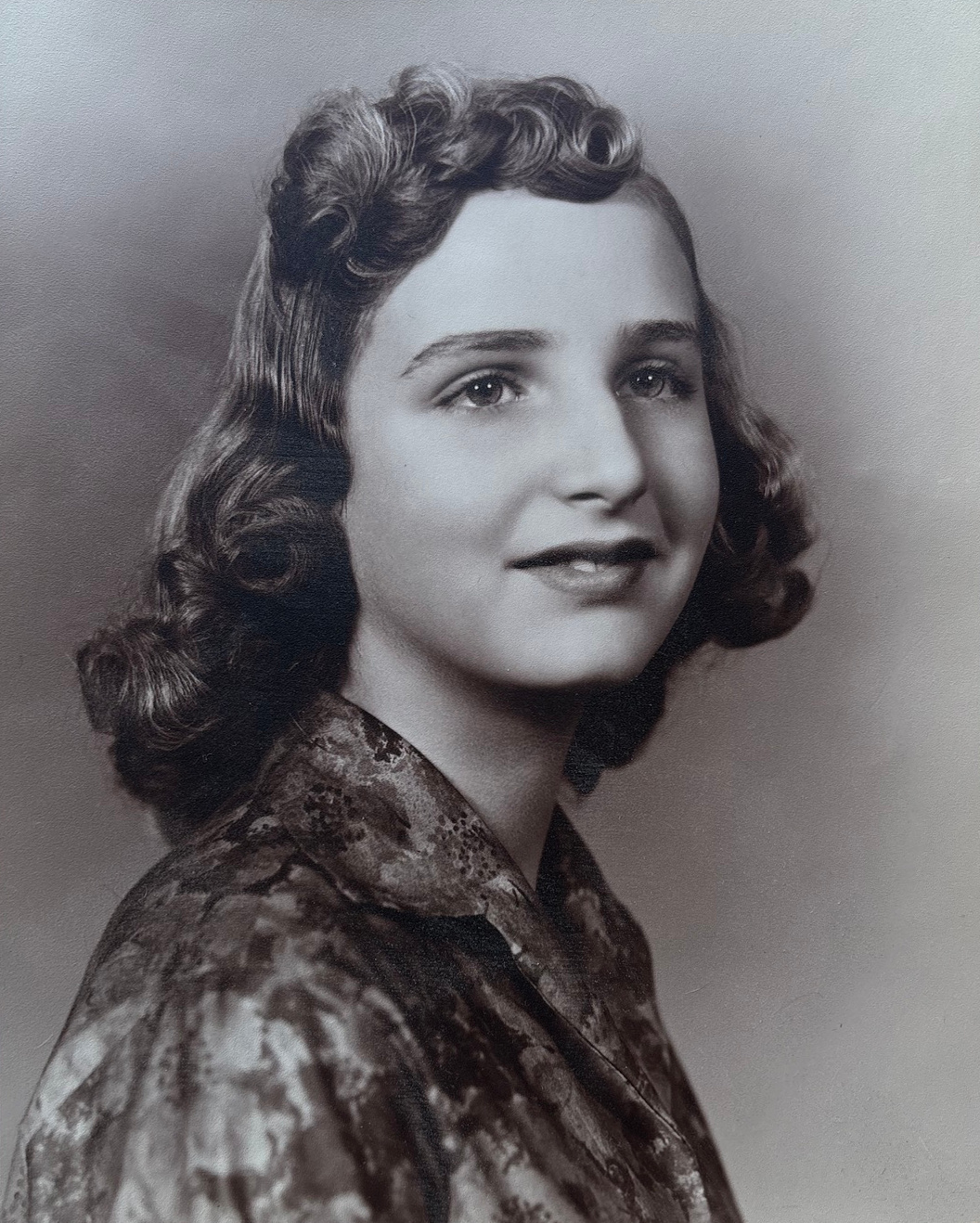 A portrait of young Linda with curled hair and a patterned blouse.