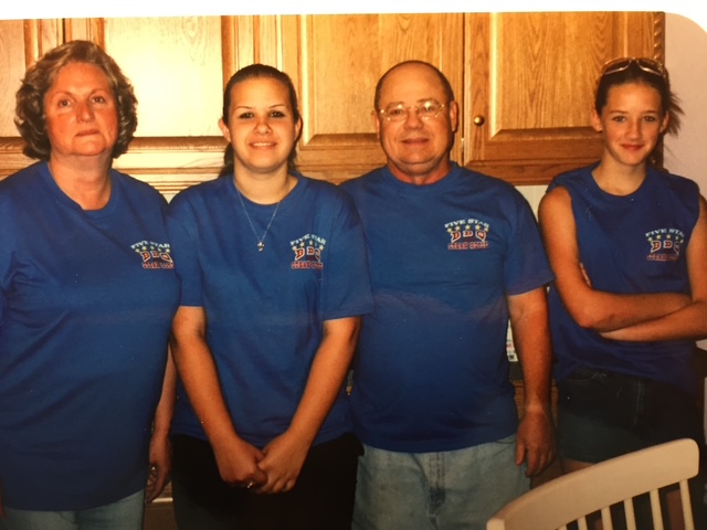 Four people standing together indoors in matching blue shirts.