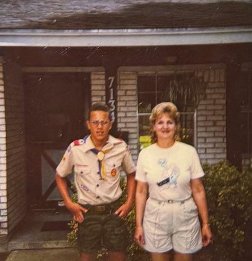Linda standing beside Jason in his Scout uniform on the front porch.