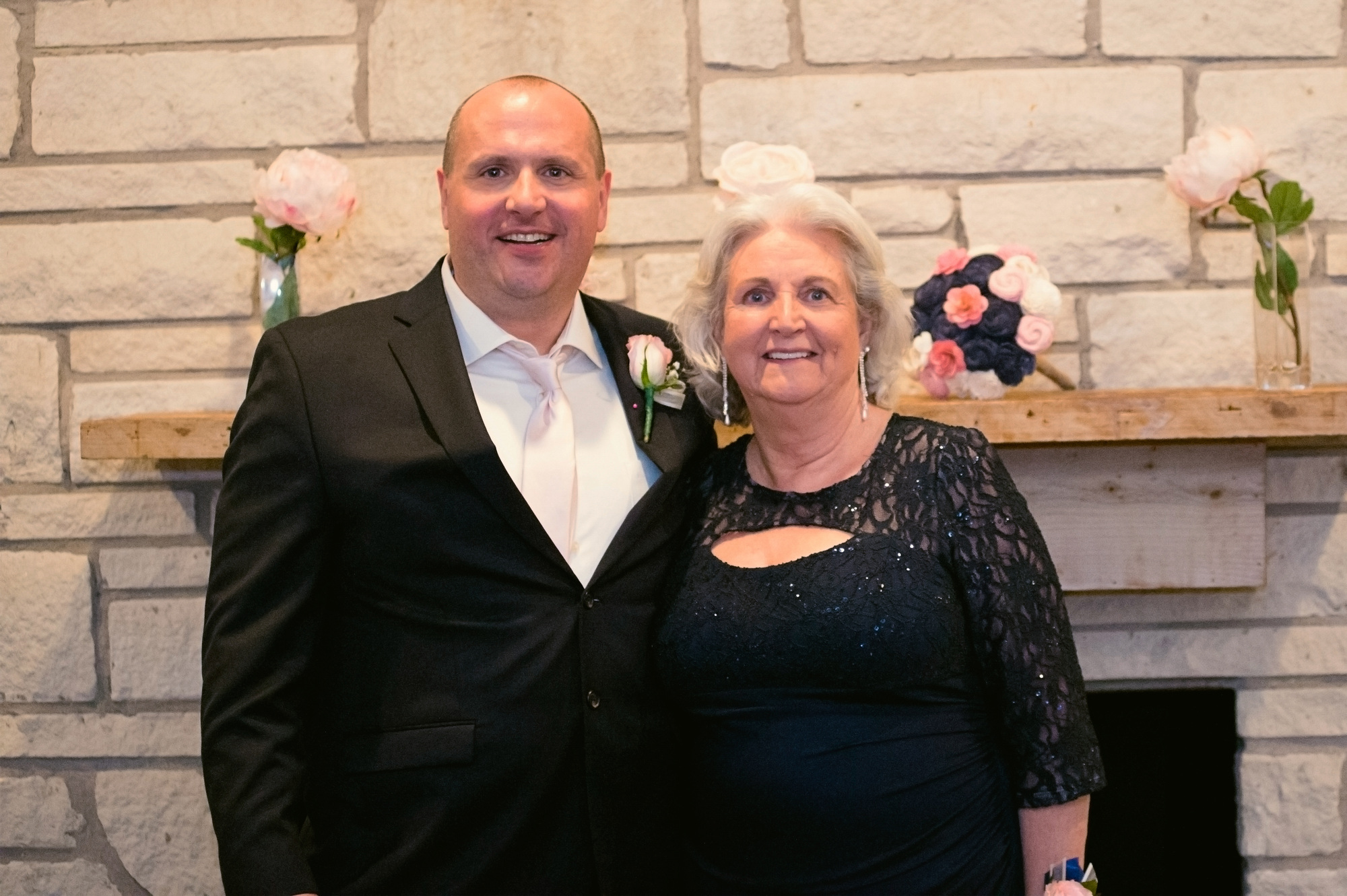 Jason and Linda smiling together beside a stone fireplace on his wedding day.