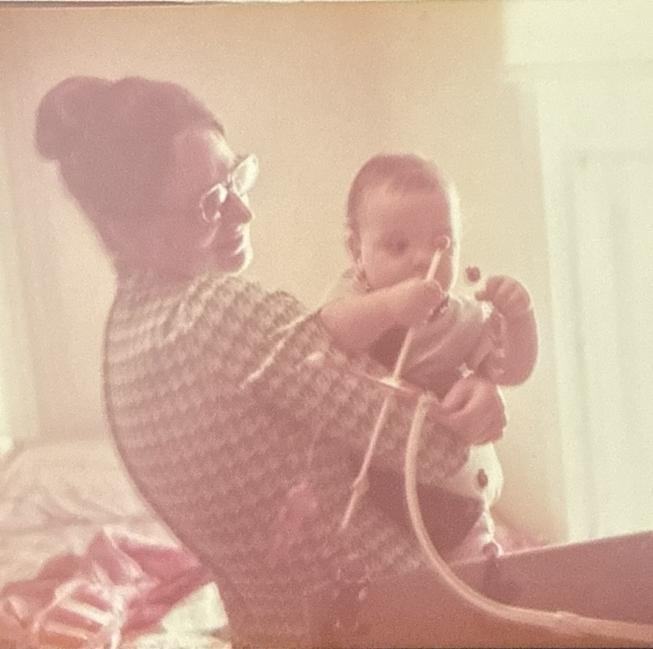 Linda in a checked dress holding Jason as a baby indoors.