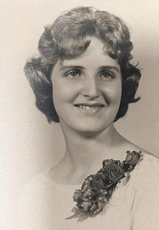 An older portrait of Linda smiling, with curled hair and a floral corsage.