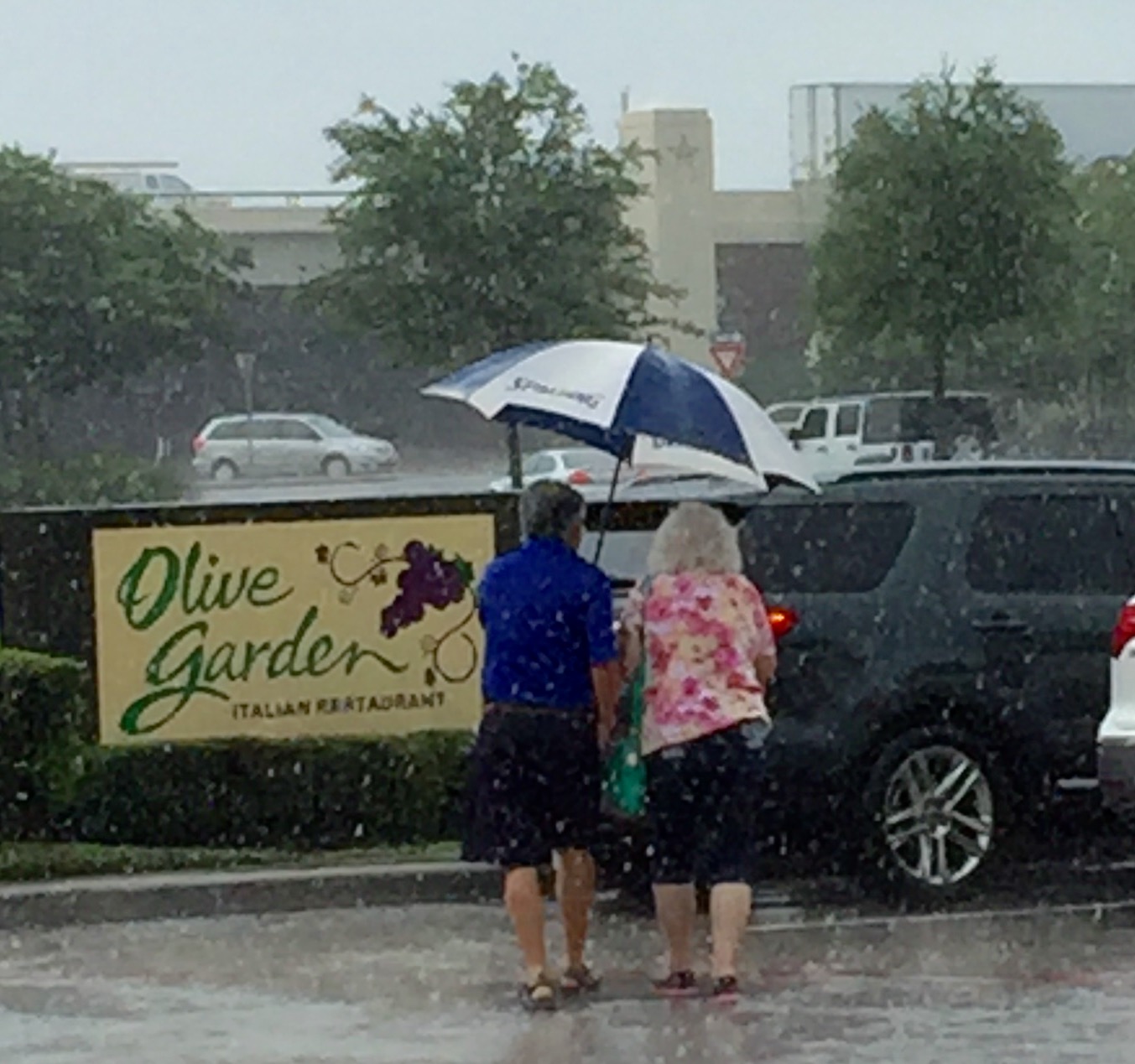 Two people sharing an umbrella in the rain outside Olive Garden.
