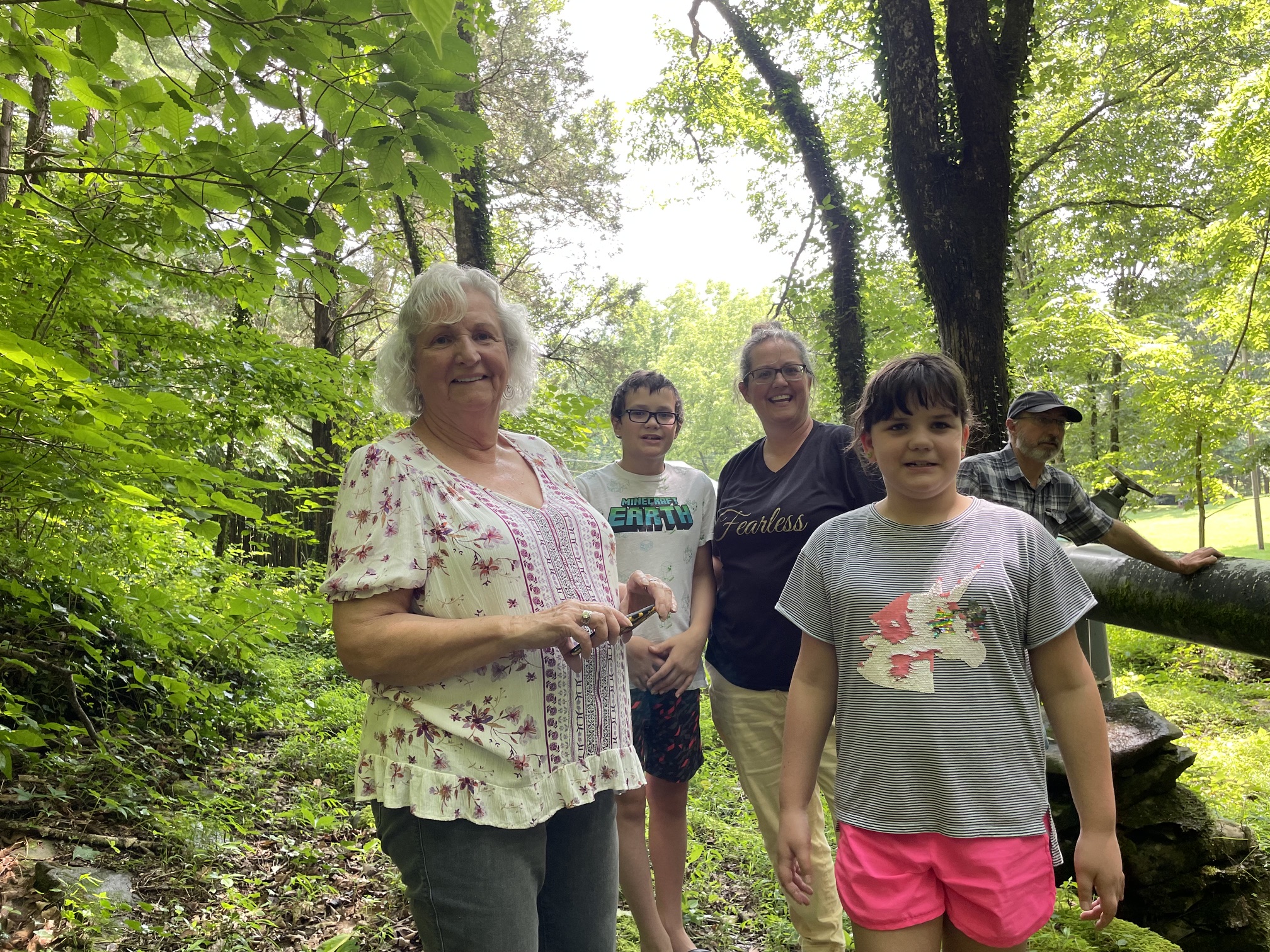 Linda with a group gathered beneath green trees.