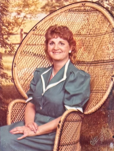 Linda seated in a wicker chair, wearing a teal dress.